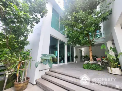 Modern home exterior with lush greenery, expansive glass windows, and a welcoming entrance, showcasing a blend of nature and contemporary design.