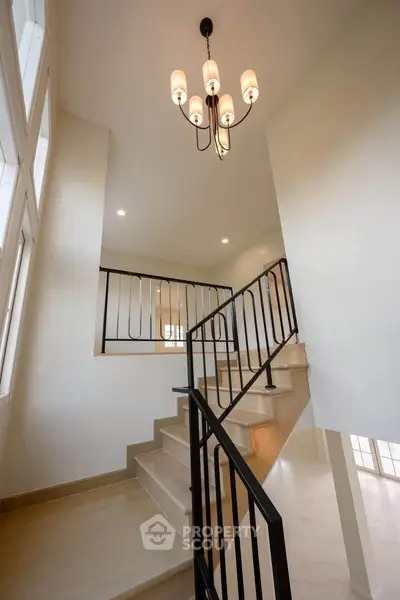 Elegant staircase with modern chandelier and sleek railing in a bright, airy home interior.