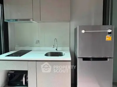 Modern kitchen with sleek appliances and minimalist design, featuring a compact fridge and electric cooktop.