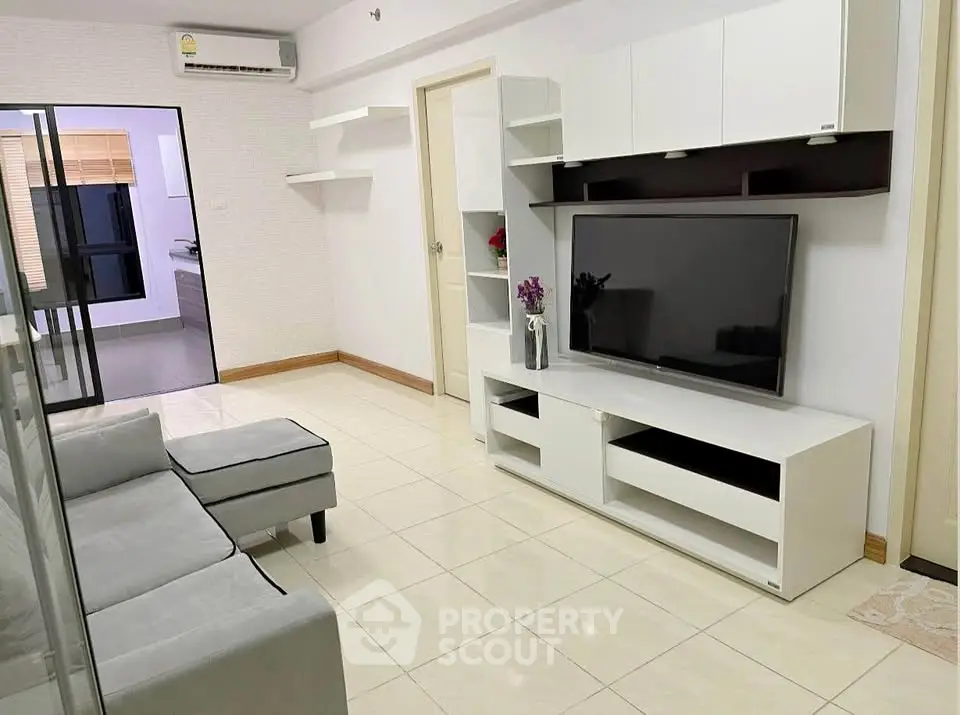 Modern living room with sleek white furniture and large TV, perfect for relaxation.