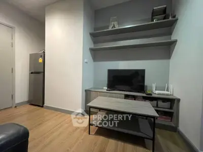 Modern living room with sleek TV stand and wooden flooring, featuring minimalist decor and a compact refrigerator.