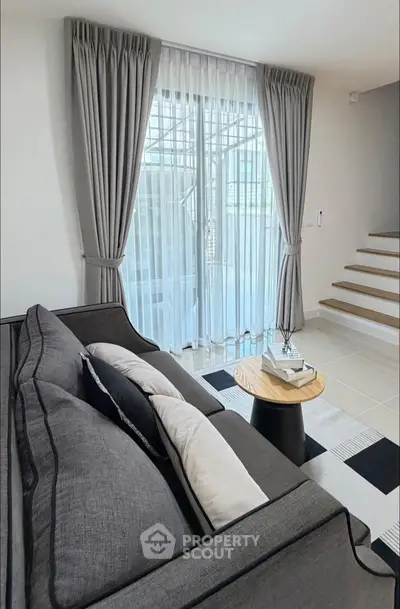 Modern living room with stylish gray sofa, elegant curtains, and sleek staircase, perfect for contemporary living.