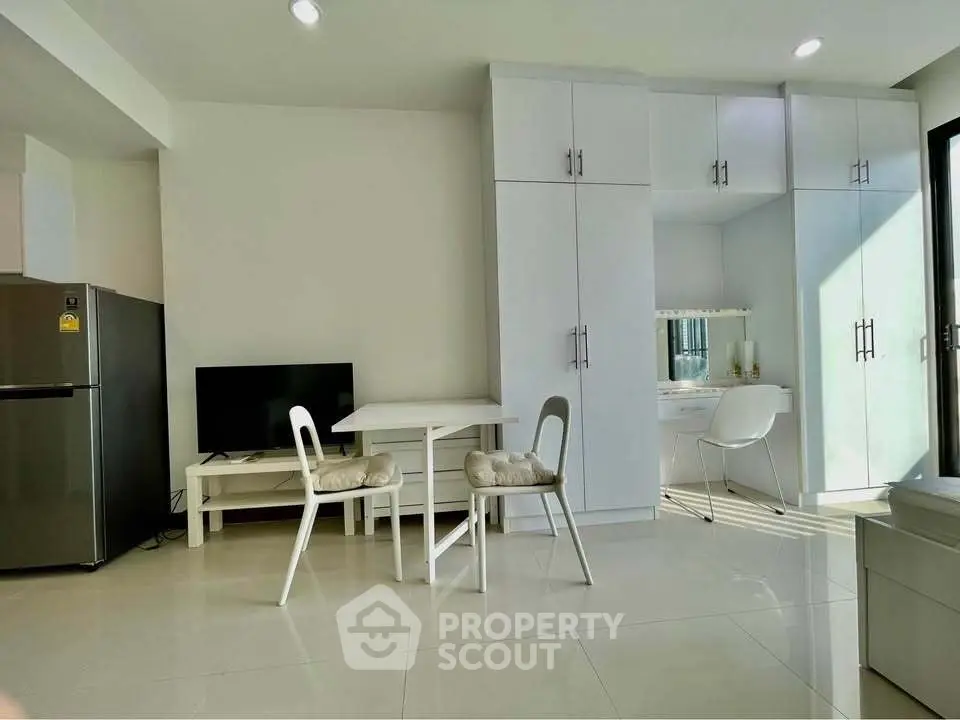 Modern living room with sleek furniture and ample natural light, featuring a compact dining area and built-in storage.