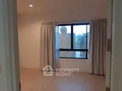 Spacious bedroom with large window and light wood flooring