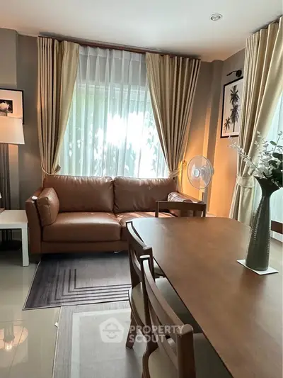 Elegant living room with leather sofa, wooden dining table, and large window with curtains.