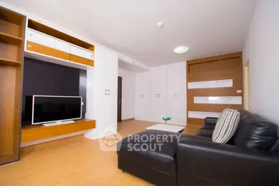 Modern living room with sleek black leather sofa and large flat-screen TV, featuring ample storage.