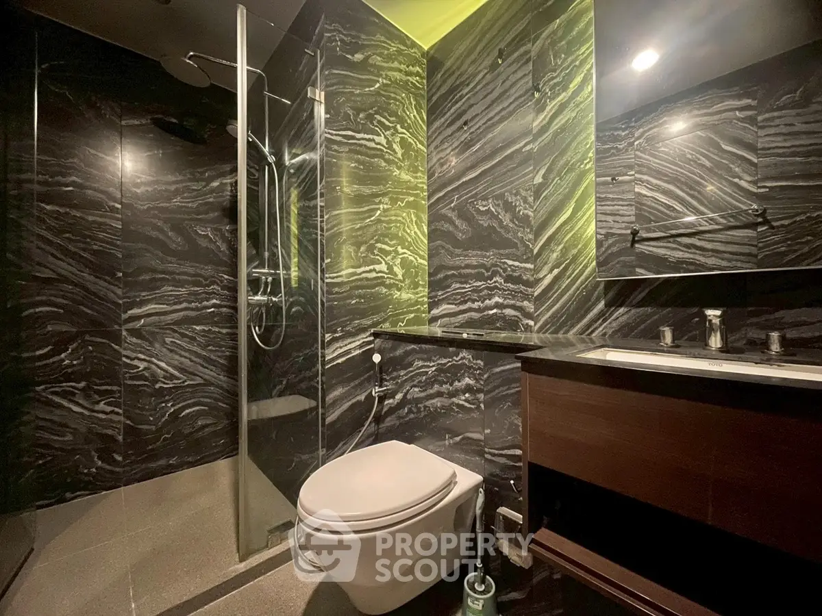 Luxurious modern bathroom with sleek black marble walls and glass shower enclosure.