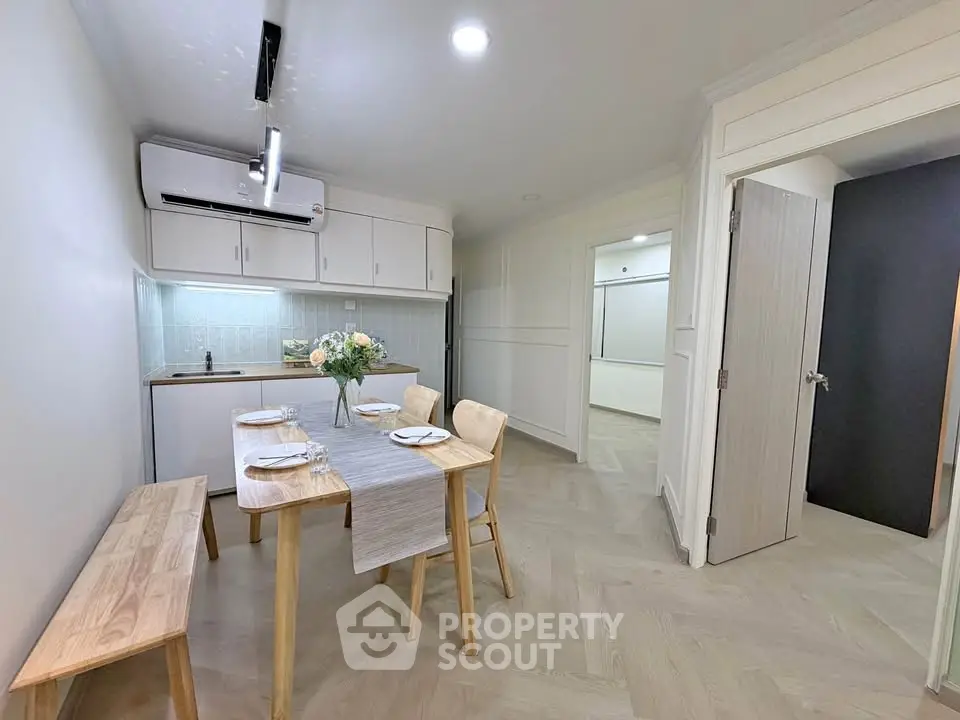 Modern dining area with wooden table and chairs, featuring a compact kitchen and stylish decor.