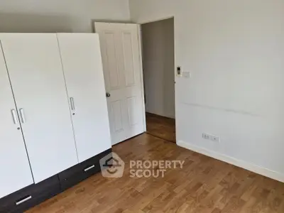 Spacious bedroom with wooden flooring and modern wardrobe in a bright apartment.