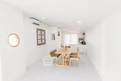 Bright minimalist dining area with wooden table and chairs, open kitchen layout, and air conditioning.