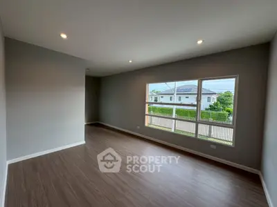 Spacious empty room with large window and wooden flooring, perfect for customization.