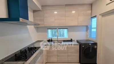 Modern kitchen with gas stove and washing machine, sleek cabinetry and natural light.