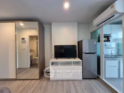 Modern living room with sleek design, featuring a TV, fridge, and air conditioning, adjacent to a stylish kitchen.