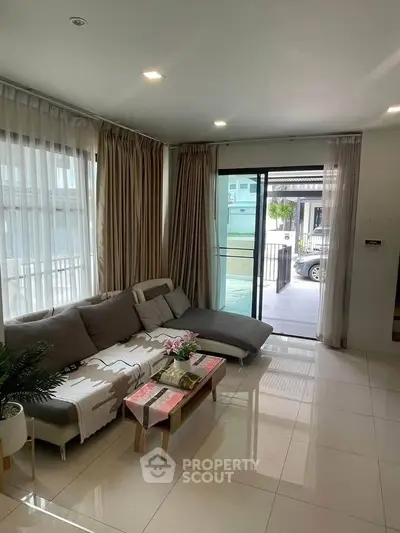 Modern living room with large windows and cozy sofa, opening to a bright outdoor view.
