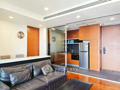 Modern living room with sleek kitchen and leather sofa in open layout apartment.