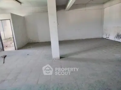 Spacious empty room with tiled flooring and a central pillar, ideal for customization.