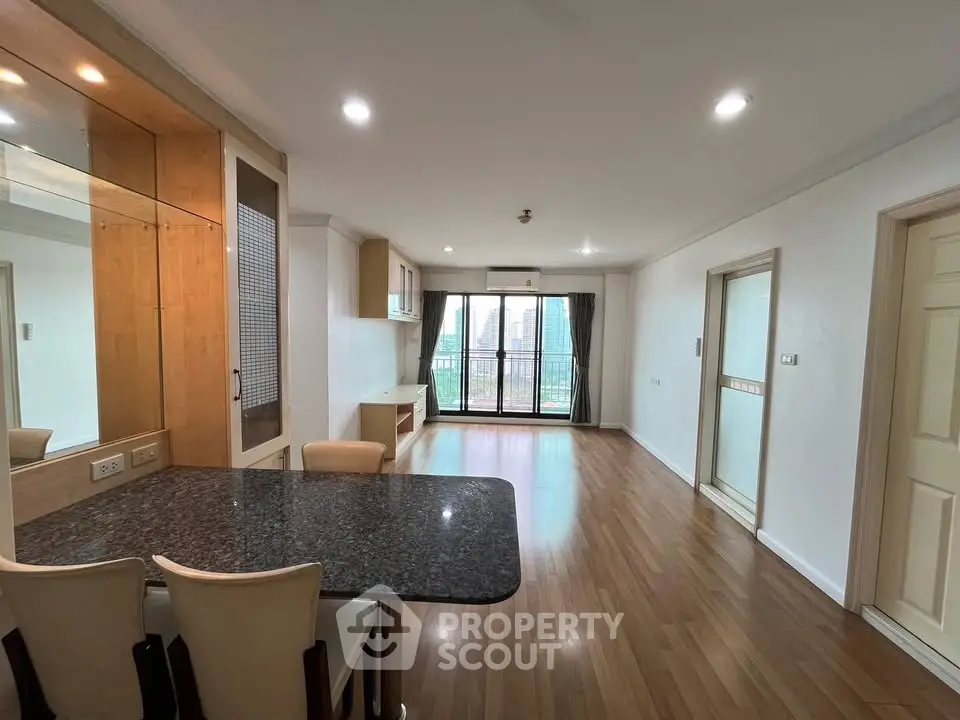 Spacious open-plan living room with wooden flooring and city view balcony.