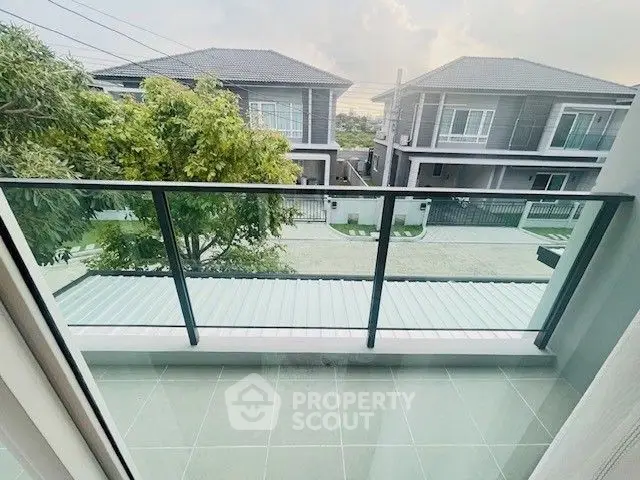 Modern balcony with glass railing overlooking suburban houses and greenery.