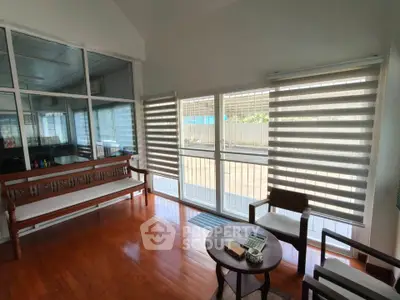 Bright living room with wooden flooring and large windows featuring modern blinds.