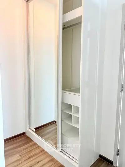Modern built-in wardrobe with mirrored sliding doors and wooden flooring in a bright room.