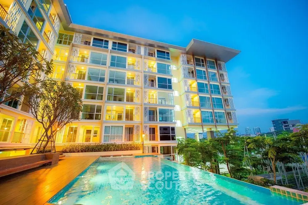 Luxurious modern apartment building with illuminated windows and a stunning pool view at dusk.