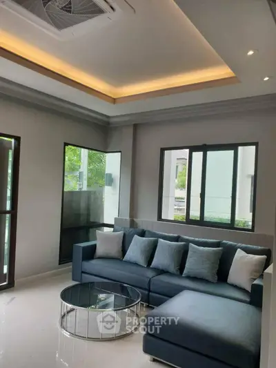 Modern living room with stylish sofa and glass coffee table, featuring large windows and elegant ceiling design.