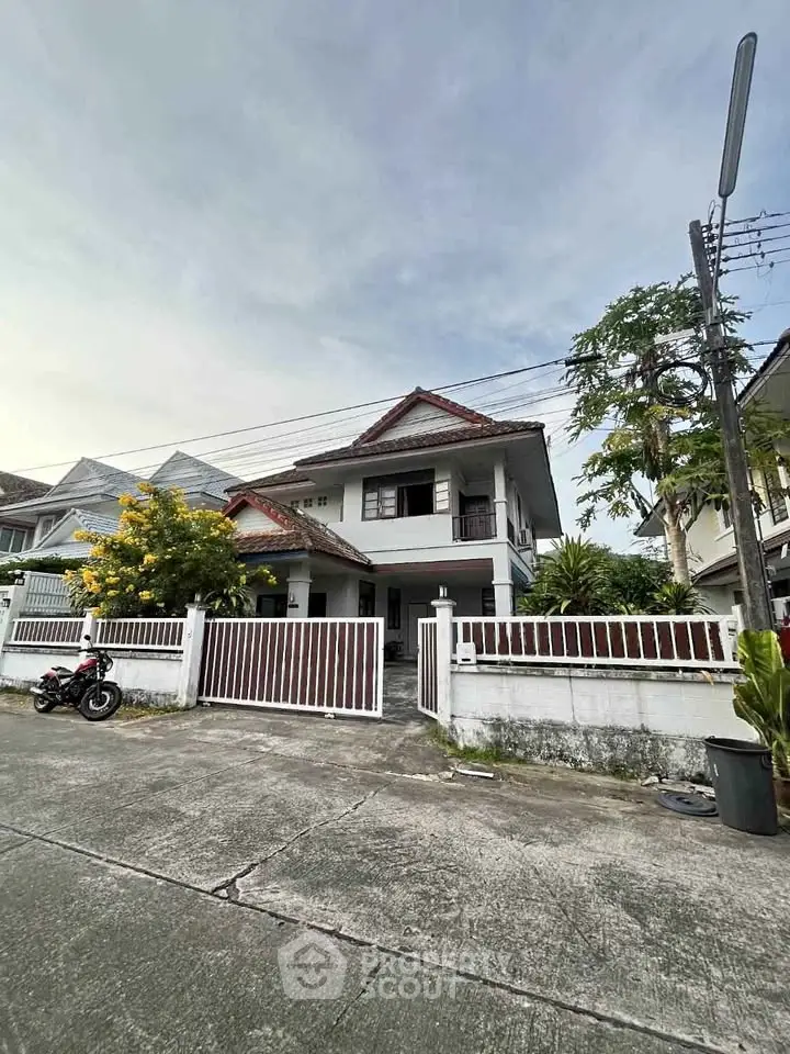 Charming two-story house with gated entrance and lush greenery in a peaceful neighborhood.