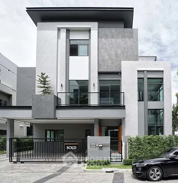 Modern multi-story house with sleek design and sold sign in front yard.