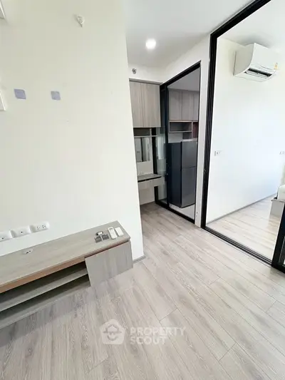 Modern apartment interior with sleek wooden flooring and built-in storage, featuring a compact kitchen area.
