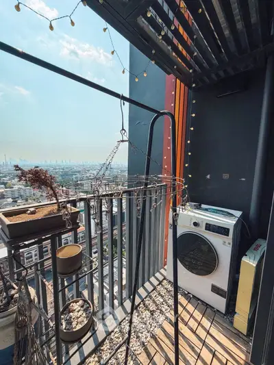 Chic urban balcony with washer, city view, and string lights, perfect for modern living.