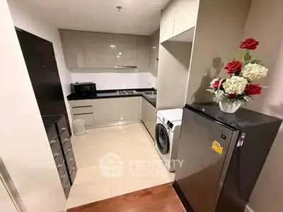 Modern kitchen with sleek cabinets, washing machine, and compact fridge in a cozy apartment.
