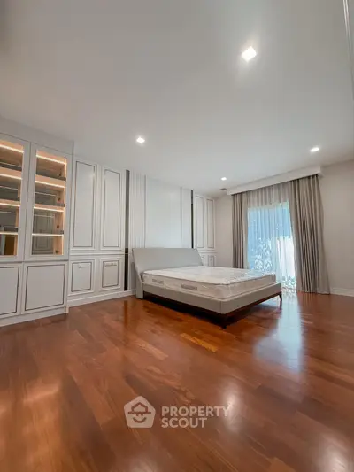 Spacious bedroom with elegant wooden flooring and large window for natural light.