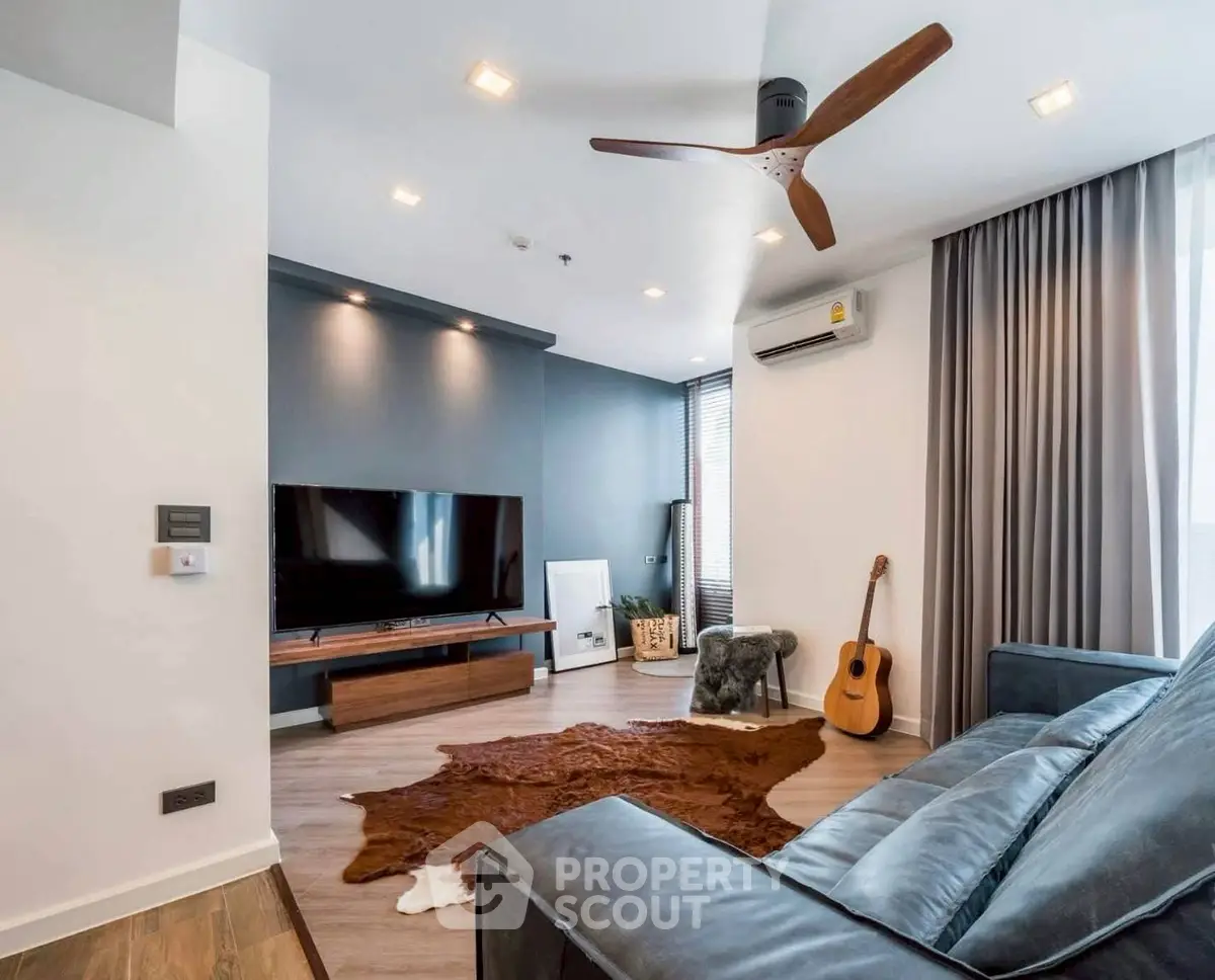 Modern living room with sleek design, featuring a TV, guitar, and stylish ceiling fan.