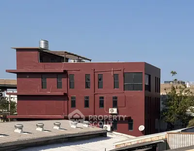 Modern red building with rooftop water tank and clear blue sky backdrop.