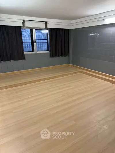 Spacious empty room with wooden flooring and large window, perfect for customization.