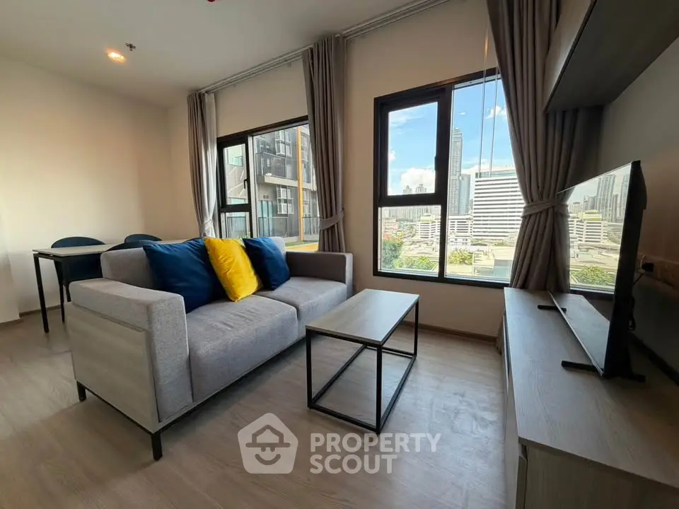 Modern living room with city view, featuring stylish furniture and large windows.