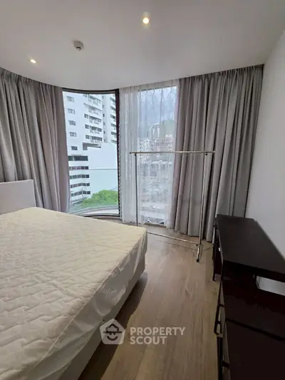 Modern bedroom with large window and city view, featuring sleek furniture and elegant curtains.