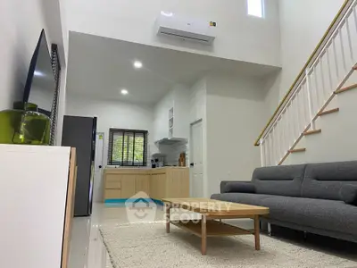 Modern living room with open kitchen, featuring sleek furniture and high ceilings.
