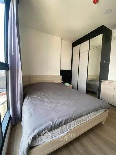 Modern bedroom with large window and sleek wardrobe in a high-rise apartment.