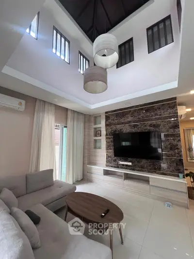 Spacious living room with high ceiling and modern decor, featuring a large TV and elegant lighting.