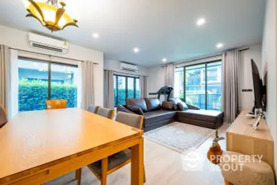 Spacious living room with modern furniture, large windows, and a cozy dining area, leading to a serene balcony with greenery.