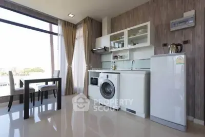 Modern kitchen with washing machine, fridge, and dining area in a bright open layout.