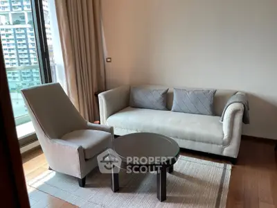 Modern living room with elegant sofa and armchair, featuring large window with city view.