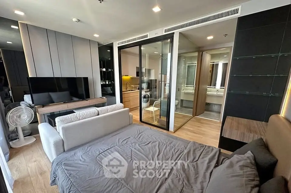 Modern studio apartment with sleek design, featuring a cozy bed, stylish living area, and glass-walled bathroom.