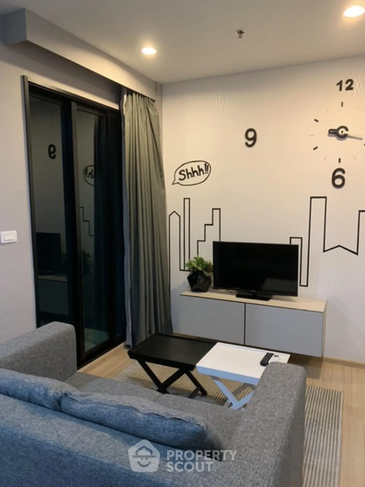 Modern living room with stylish decor and wall clock, featuring a cozy sofa and TV setup.