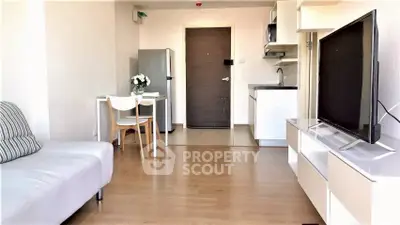 Modern living room with sleek furniture and open kitchen layout, featuring a large TV and stylish decor.