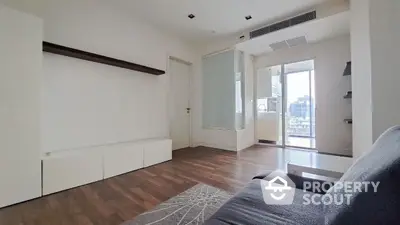 Spacious and modern living room with natural light flooding through large balcony doors, featuring sleek hardwood flooring and a contemporary design aesthetic.