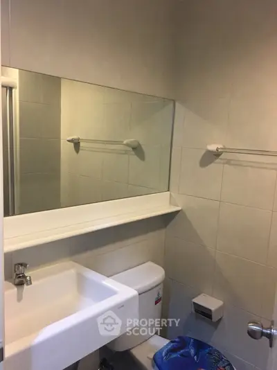 Compact bathroom with modern fixtures and neutral tiles, featuring a large mirror and a sleek sink.