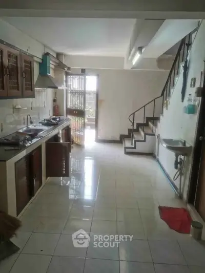 Spacious kitchen with open layout and staircase, featuring tiled flooring and ample natural light.