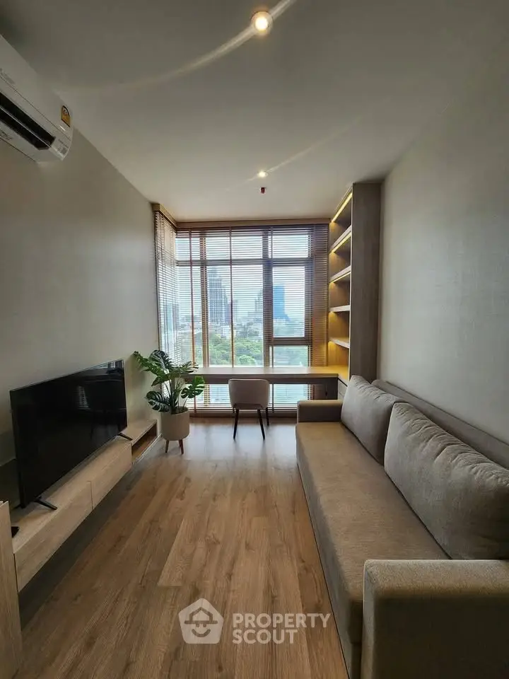 Modern living room with large window and city view, featuring a cozy sofa and sleek TV setup.